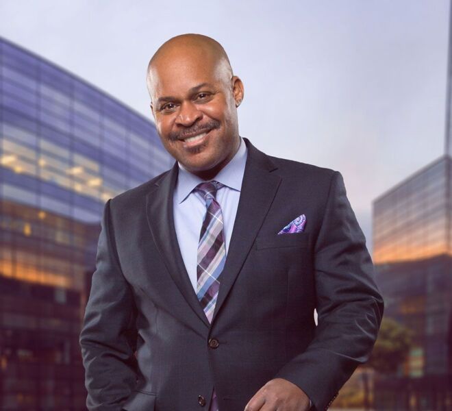 businessman in an urban portrat wearing grey suit and lavender shirt with office buildings in background. smiling with one hand in pocket