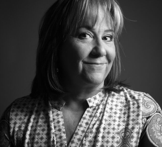 medical professional with checkered top poses with head to the side, looking back smiling at camera in black and white portrait