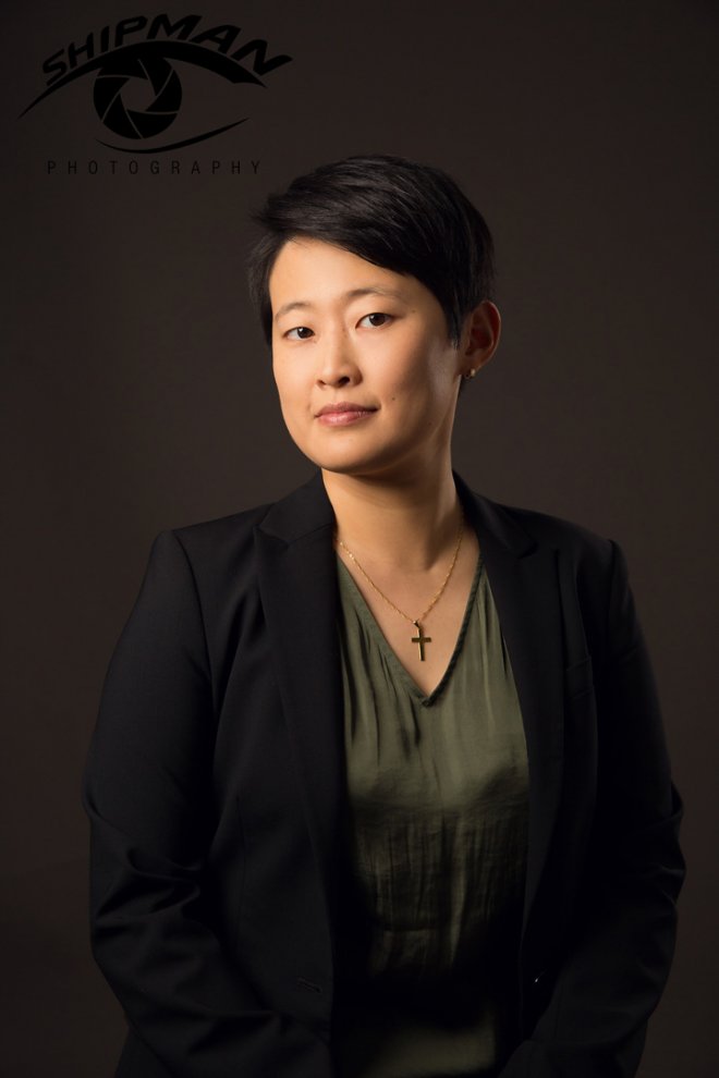 female surgeon from university of oklahoma wearing black jacket and green top poses on brown background with short black hair and slight smile