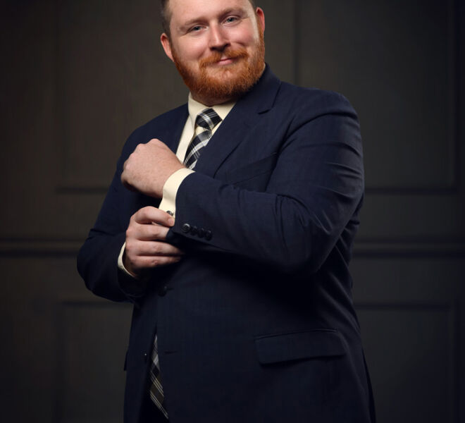man in a blue suit smiling and adjusting his cuff with wood panel background