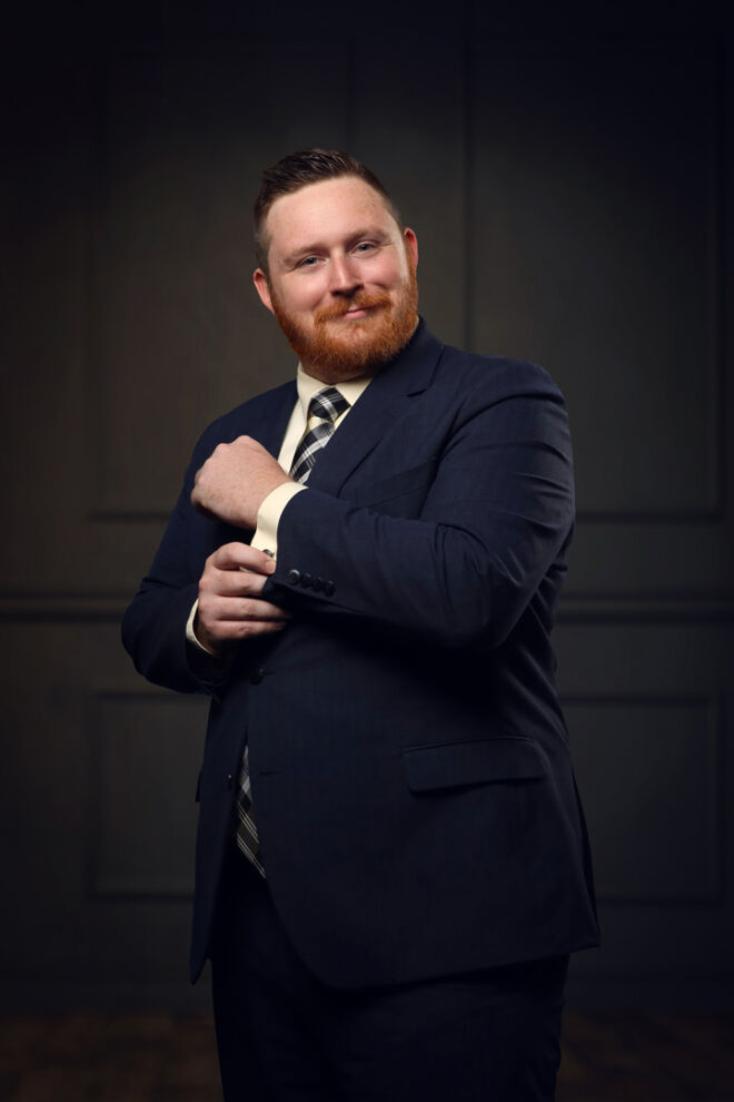 man in a blue suit smiling and adjusting his cuff with wood panel background