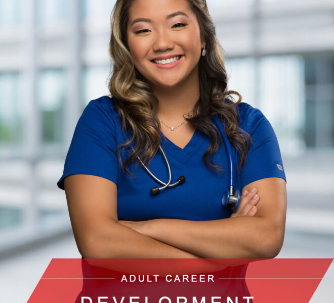 nurse in blue scrubs poses smiling with arms crossed and hospital background behind