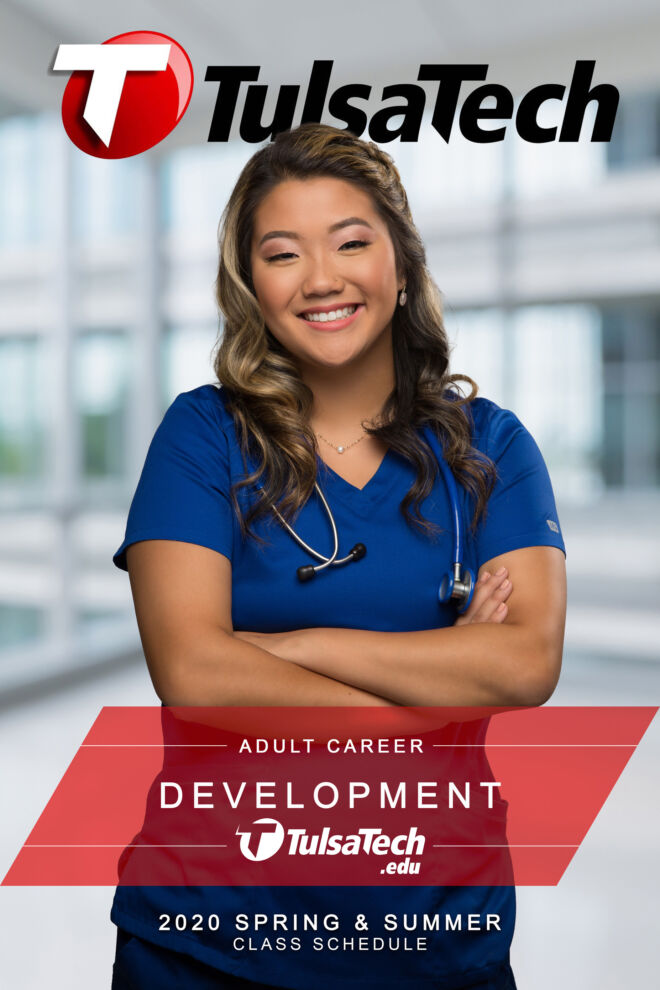 nurse in blue scrubs poses smiling with arms crossed and hospital background behind