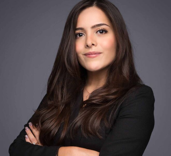 attractive young brunette female attorney in black suit, with arms crossed and slight smile. on a grey background