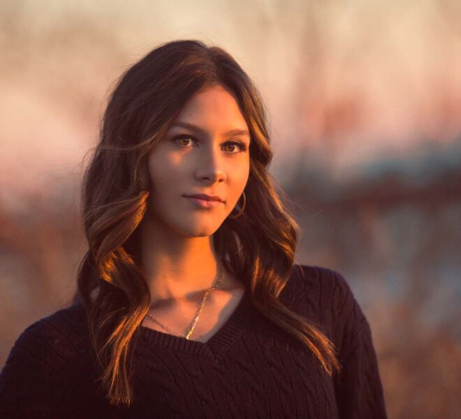 Young woman in golden hour sunset light outdoors by the river with black sweater