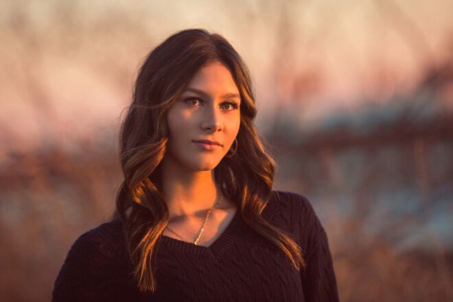 Young woman in golden hour sunset light outdoors by the river with black sweater