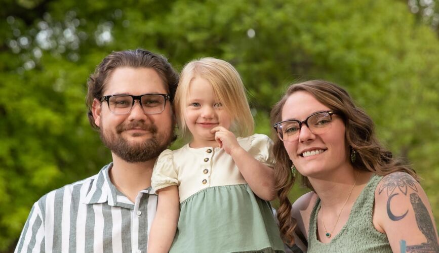 smiling baby with young parents pose for family photo in Tulsa's woodward park