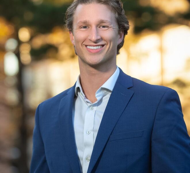 handsome blonde businessman in a blue suit and light blue shirt poses in a fall foliage park setting smiling for headshots