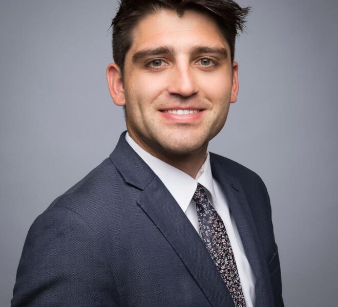 young tulsa attorney in a grey suit and black hair poses smiling for his headshot on a grey background
