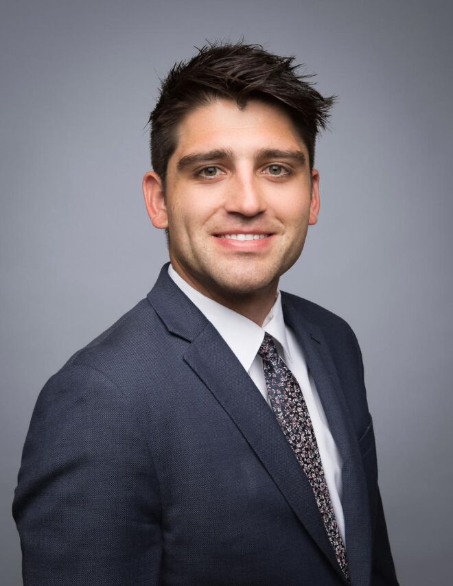young tulsa attorney in a grey suit and black hair poses smiling for his headshot on a grey background
