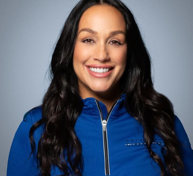 Smiling nurse in a blue pullover with long black hair poses smiling on a grey background