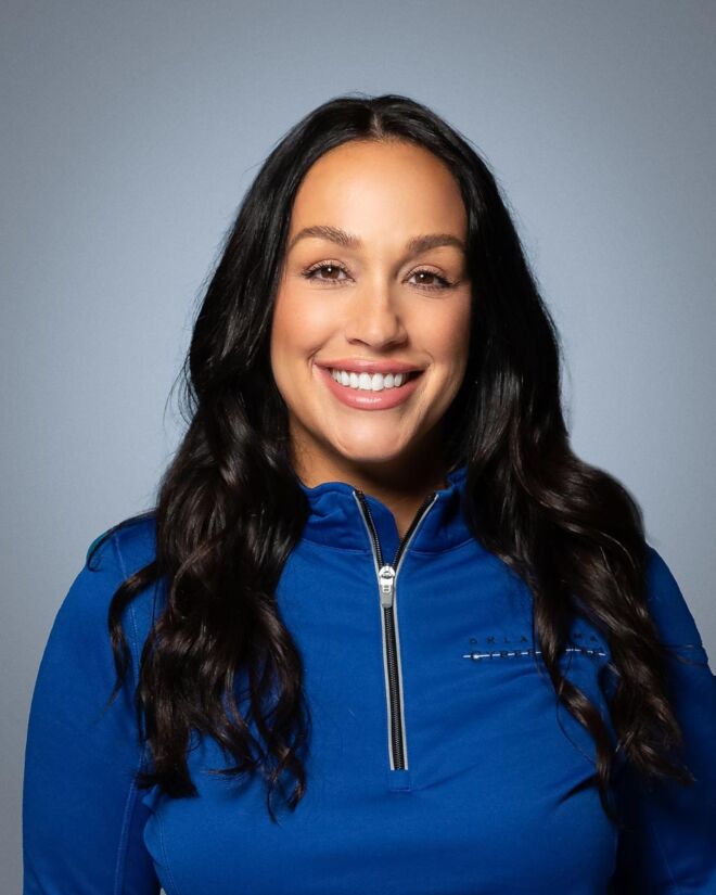 Smiling nurse in a blue pullover with long black hair poses smiling on a grey background