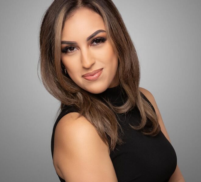 Young female tulsa realtor in black dress, smiling for headshots on a grey background