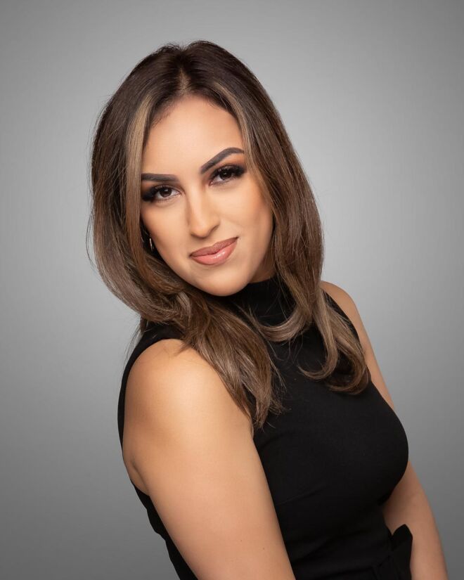 Young female tulsa realtor in black dress, smiling for headshots on a grey background