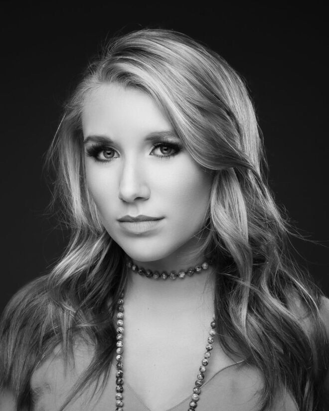 black and white headshot of a beautiful young female singer with long blond hair, wearing a serious look and a pearl necklace on a dark background