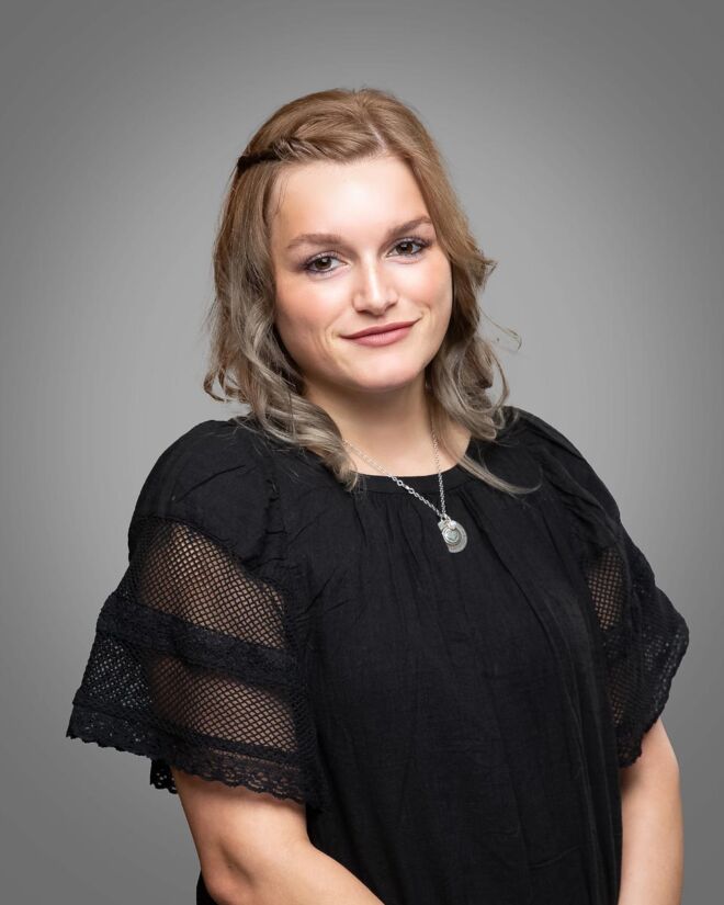 young professional woman with blonde hair and a black dress smiles for a photo on a grey background