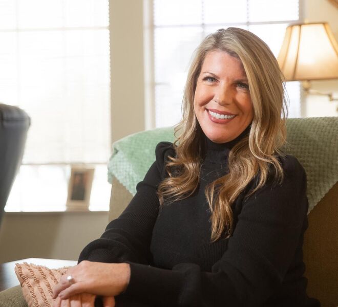 pretty blonde therapist sitting smiling at her office desk, wearing a black dress