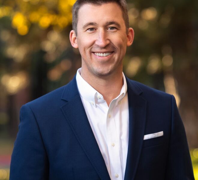 businessman in a blue jacket and white shirt poses smiling in a park setting