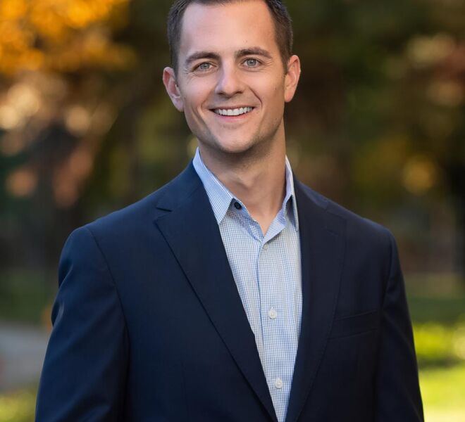 Smiling businessman in a blue suit jacket and no tie poses in a Tulsa park during the fall