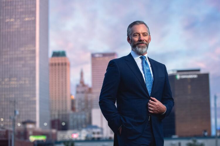 Tulsa attorney in blue suit standing with downtown in background
