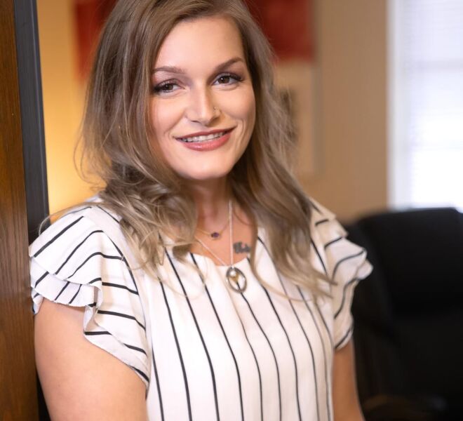Blonde therapist with a smile, wearing a white top, poses in the doorway of her office for headshots in Tulsa