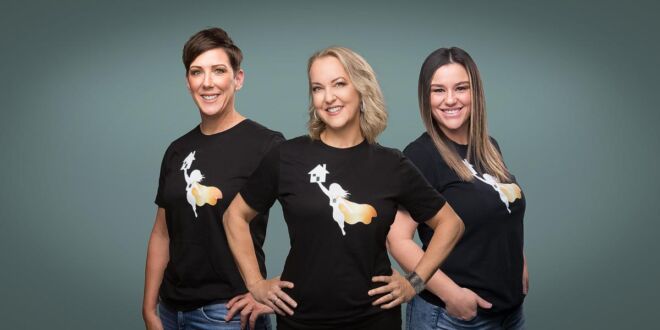 three business partner women standing together in a branding photo, wearing matching logo'ed black shirts on a green studio background