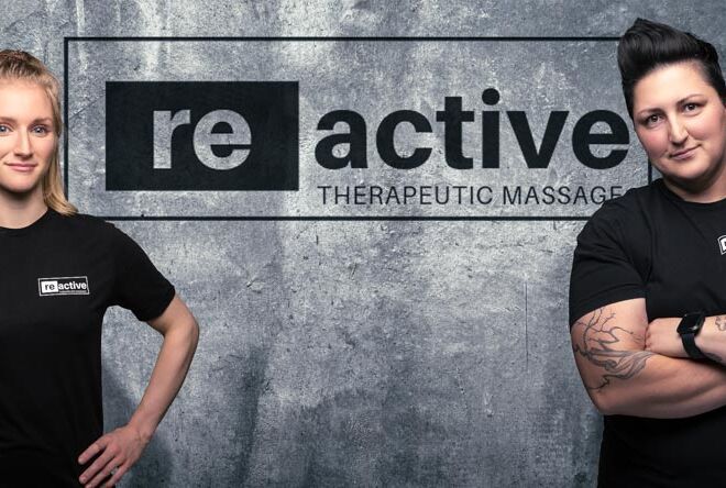 Two woman business teammate pose in front of their logo branded wall