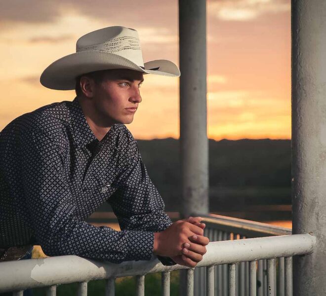 handsome young man in a cowboy hat looking out over a balcony on a lake at sunset
