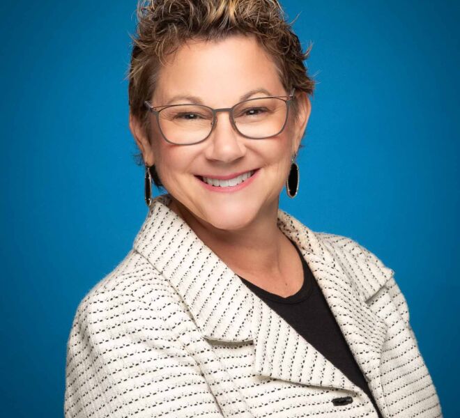 smiling businesswoman wears glasses and short hair, with a white houndstooth jacket and black top, on a blue background
