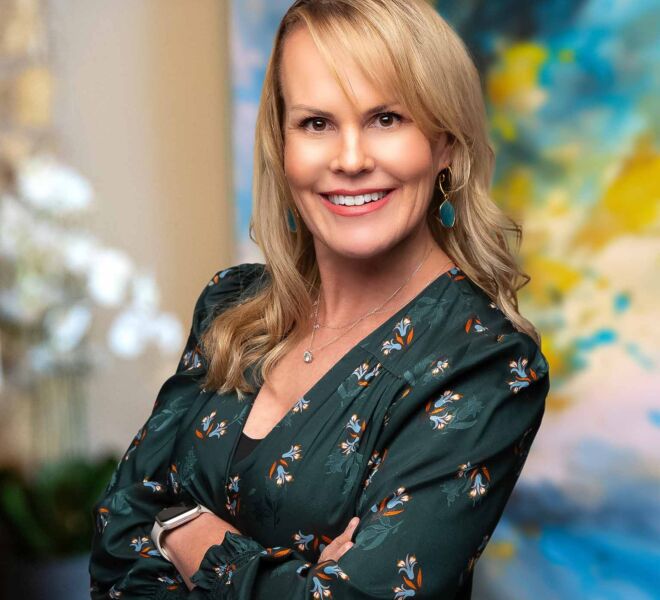 Blonde businesswoman in a green dress, smiles and poses for headshots in front of an office background