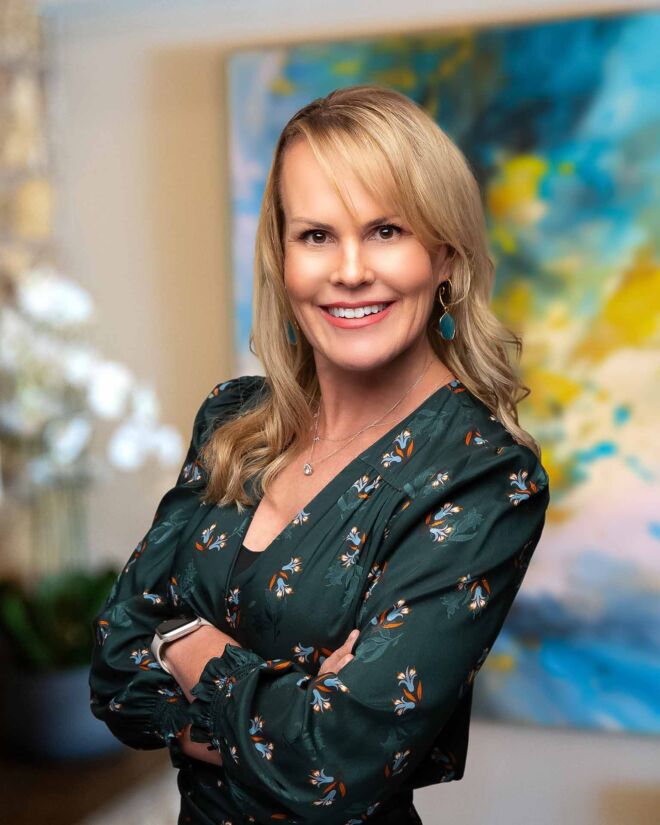 Blonde businesswoman in a green dress, smiles and poses for headshots in front of an office background