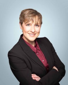 professional woman on light blue studio headshot background smiling with arms crossed