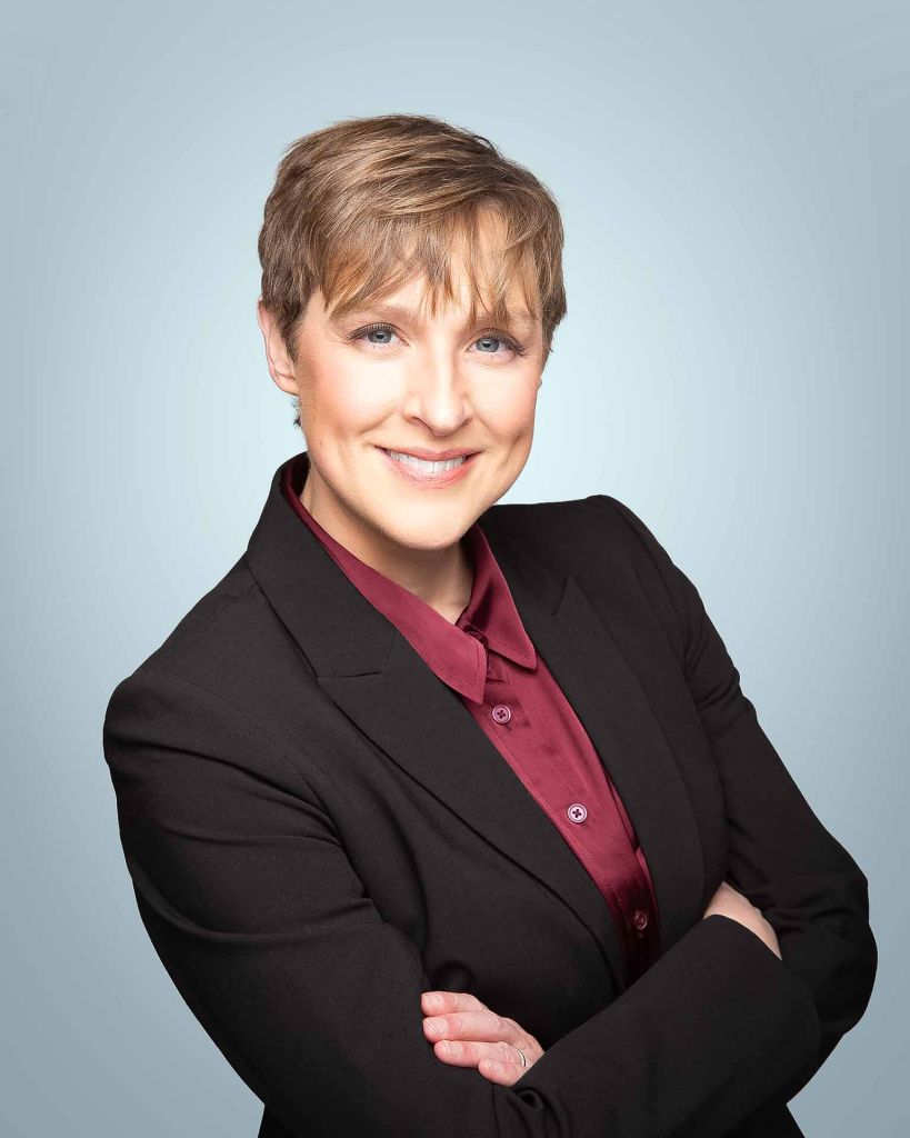 professional woman on light blue studio headshot background smiling with arms crossed
