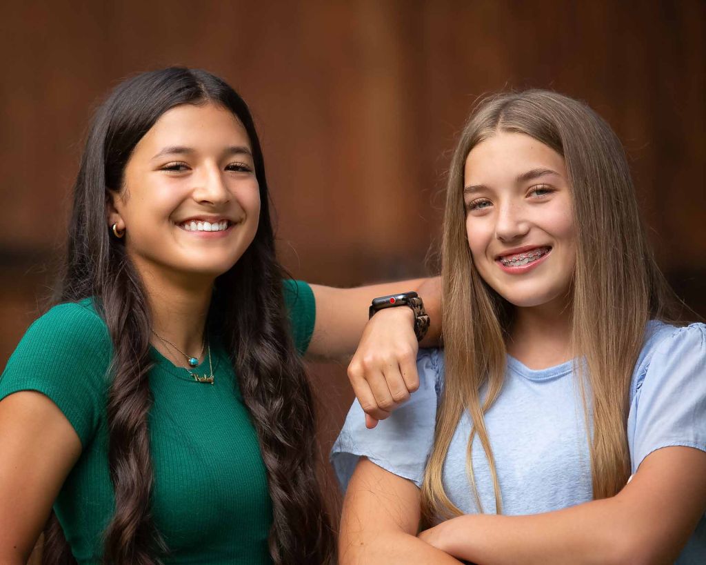 two girls posing in front of barn door smiling with perfect teeth because of braces. commercial professional photography Bixby