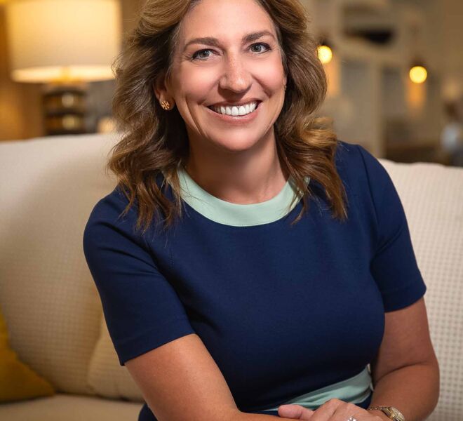 Attractive businesswoman in a blue dress, sitting smiling on a tan couch in an office setting in Tulsa