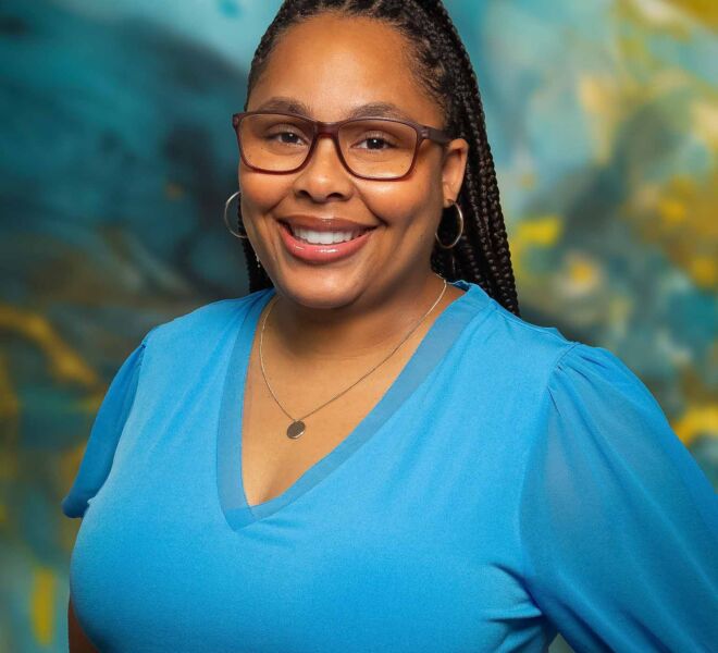 African American businesswoman in glasses and a blue top, smiles and poses for headshots in front of a blue and gold background