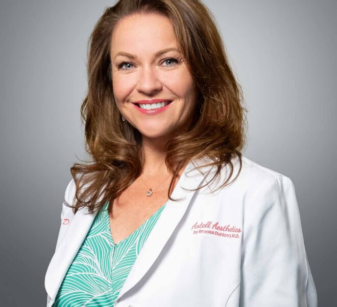 Pretty female doctor in a white lab coat and green dress, smiling on a grey portrait background
