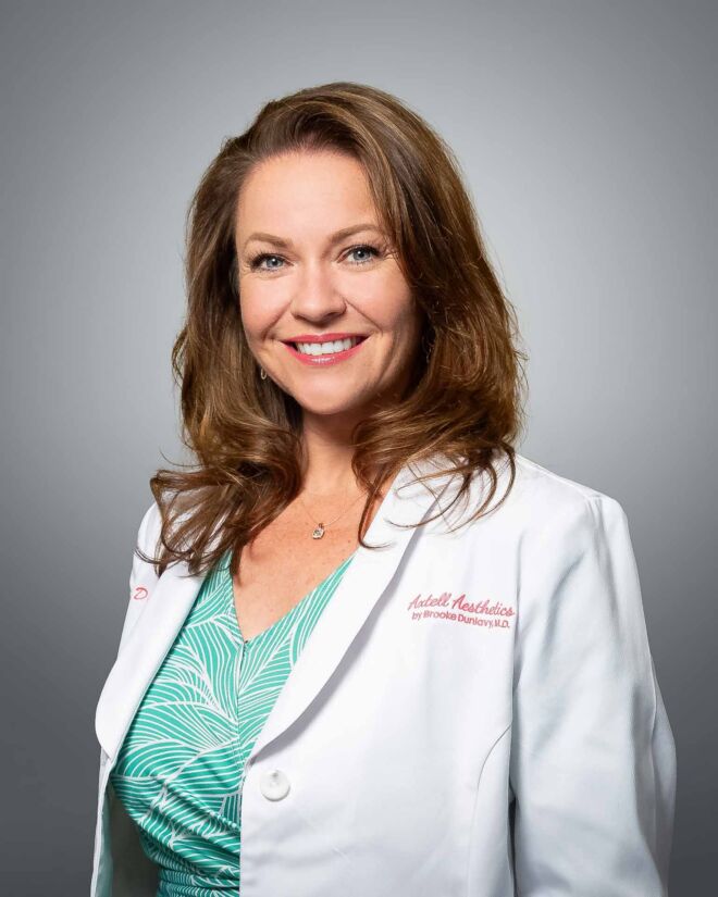 Pretty female doctor in a white lab coat and green dress, smiling on a grey portrait background