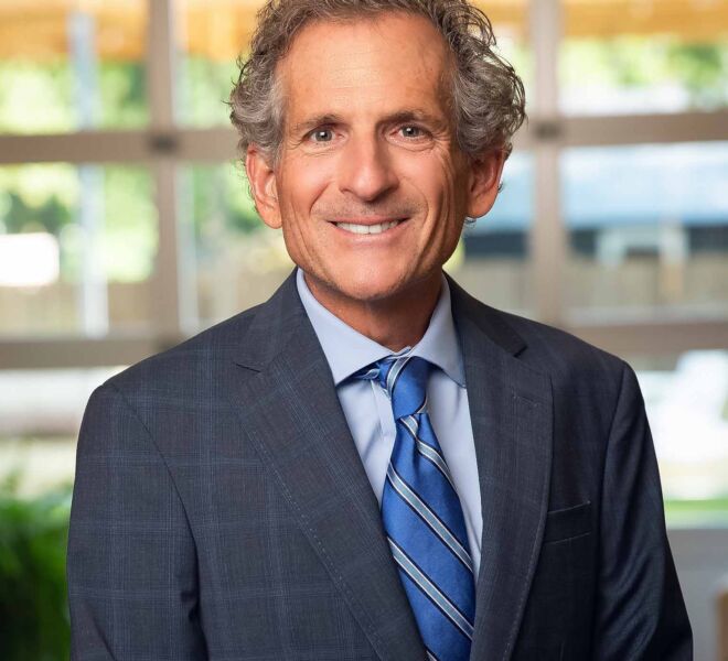 Businessman in a grey suit and blue tie smiling for a headshot in an office