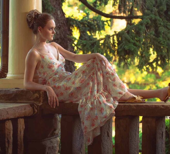 young woman posing on the porch of a victorian era home in the sunlight