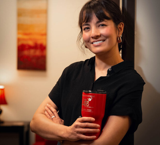 Smiling female therapist, holding a red coffee mug, standing in the doorway of her office.