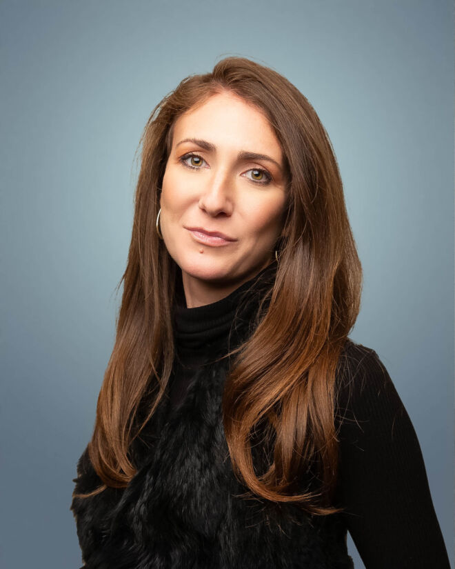 Pretty female lawyer in a black vest posing for headshots on a blue background