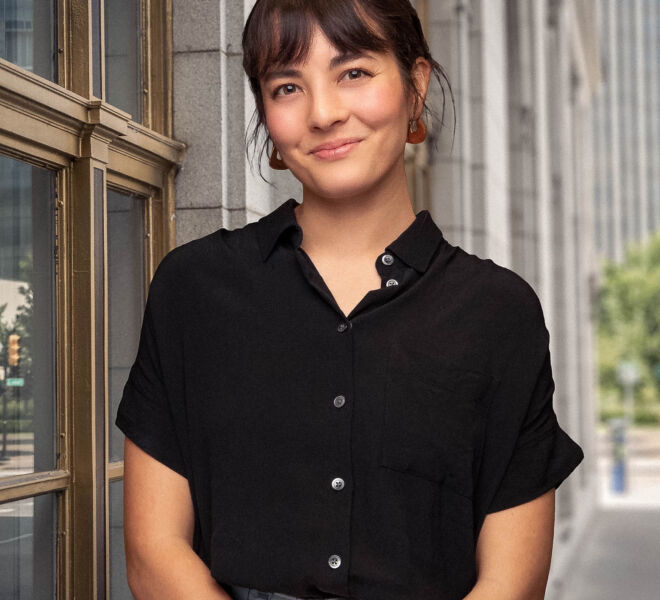 Pretty girl in a black top, smiling for a headshot on a downtown Tulsa sidewalk