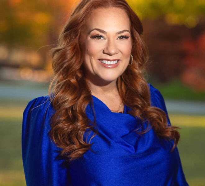 Attractive red haired Tulsa businesswoman in a blue top, smiling outdoors in a park full of fall colors