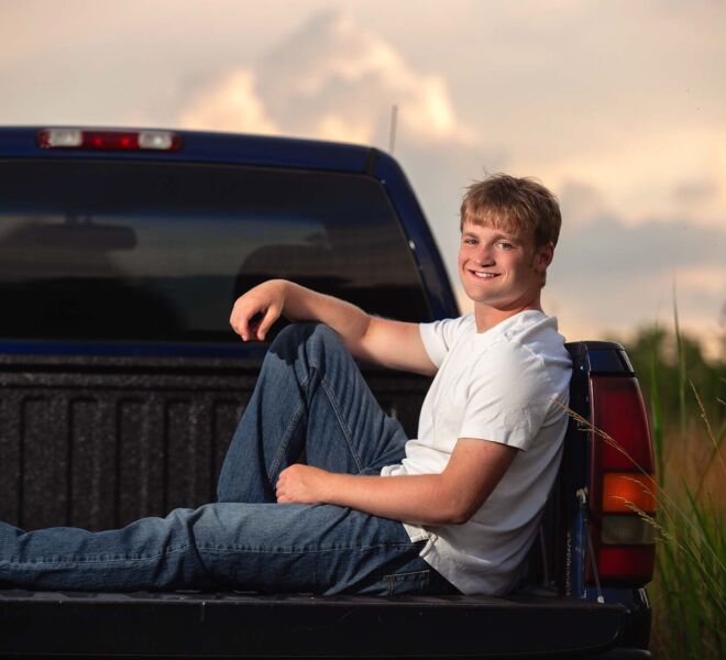 young man sitting in the back of his truck in a field at sunset