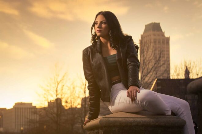 young woman sitting on a bridge in a park with downtown behind her