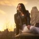 young woman sitting on a bridge in a park with downtown behind her