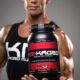 muscular man smiles and holds a jar of workout supplement powder in a product photo