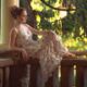 young woman posing on the porch of a victorian era home in the sunlight