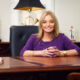 Happy female doctor sitting at her desk, smiling, wearing a purple dress
